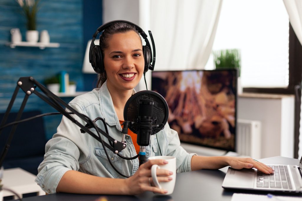 Smiling influencer woman sitting in front of camera recording video blog for fashion blog